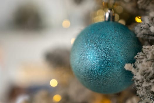 A blue Christmas ornament hanging from a tree. The ornament is shiny and has a glittery surface