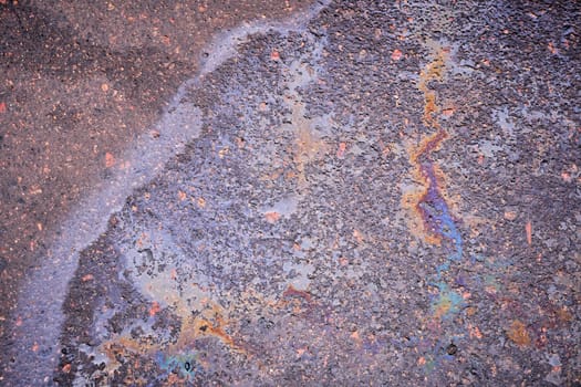 Oil or gasoline leaking from under a car in the rain on the asphalt in a parking lot. Detail of an oil stain on the asphalt of a wet road