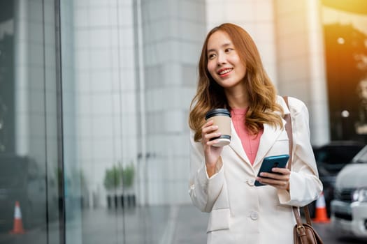 A smart businesswoman stays connected on the go with her smartphone and a cup of coffee. She is navigating the busy city with ease.