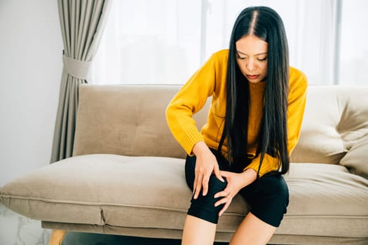 Close-up of a young woman holding her painful knee on a sofa suffering from chronic tendon arthritis. Reflecting Health Care and Medical Concept emphasizing tendon inflammation and pain.