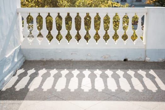 A balcony with a railing and a tree in the background. The railing is white and has a shadow on it