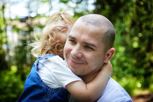 Gentle Father Holding Young Daughter Outdoors in Daylight. A tender moment as dad embraces his little girl in a sunny garden