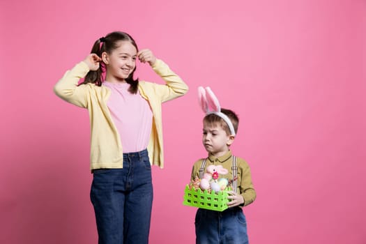Little kids posing with festive handmade decorations for easter celebration, feeling excited about spring holiday tradition. Sweet brother and sister showing painted eggs in a basket.