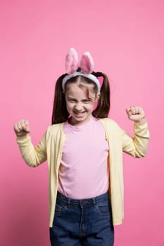 Angry irritated young girl expressing her disappointment in studio, wearing bunny ears buy feeling displeased about something. Little toddler shows her disapproval, negative emotions.
