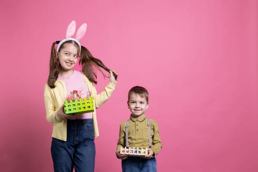 Positive cute children presenting festive handmade ornaments on camera, feeling joyful about easter holiday event and spring time. Brother and sister show their baskets with painted eggs.