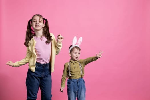 Sweet little kids having fun with dance moves in studio, fooling around and feeling happy about easter holiday festivity. Adorable toddlers siblings dancing in front of camera, bunny ears.