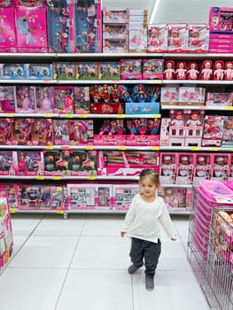 Little girl is walking through a supermarket with many dolls on the shelves. High quality photo