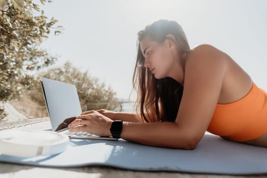 Digital nomad, Business woman working on laptop by the sea. Pretty lady typing on computer by the sea at sunset, makes a business transaction online from a distance. Freelance, remote work on vacation