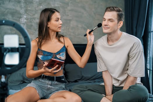 Young woman making beauty and cosmetic tutorial video content for social media using her boyfriend as model and light ring. Beauty blogger showing how to beauty care to audience or follower. Unveiling