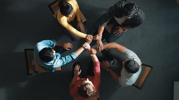 Top down aerial view of diverse business people hold wrist while sitting circle together. Faithful prayers holding wrist or hand of each other. Represented teamwork, unity, togetherness. Symposium.