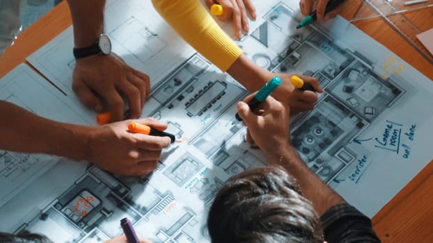 Top view of civil engineer team writing at blueprint at meeting table with color palettes. Group of smart diverse people planning and taking a note while manager looking at project plans. Symposium.