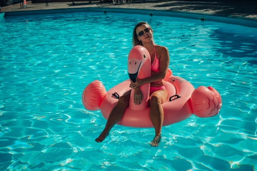 A woman is sitting on a pink inflatable flamingo in a pool. Concept of fun and relaxation, as the woman is enjoying her time in the water