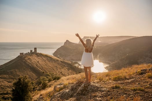 A woman is standing on a hill overlooking a body of water. She is wearing a white dress and she is happy