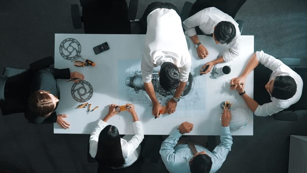 Top down aerial view of smart engineer team working together to design turbine engine. Professional technician discussing about jet engine construction while pointing at part of engine. Alimentation.