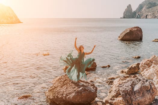 Woman green dress sea. Woman in a long mint dress posing on a beach with rocks on sunny day. Girl on the nature on blue sky background