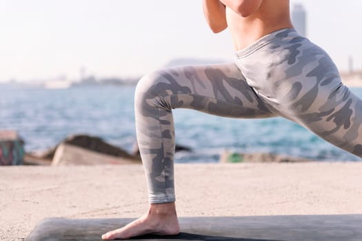 cutout of the leg of unrecognizable woman in sportswear practicing yoga by the sea, relaxation and healthy lifestyle concept