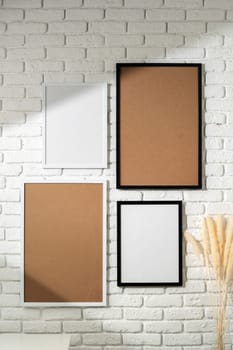 Several empty photo frames of different sizes and colors are displayed in an asymmetrical arrangement against a textured white brick wall, potentially signifying a modern and minimalist interior design approach. A small portion of a green plant is visible, injecting a touch of nature into the scene.