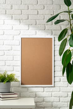 A blank photo frame is mounted on a white brick wall, ready for a personalized image. A stack of books and a vibrant houseplant rest on a white shelf, adding a touch of coziness and life to the modern minimalist decor.