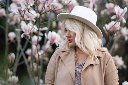 Magnolia flowers woman. A blonde woman wearing a white hat stands in front of a tree with pink flowers