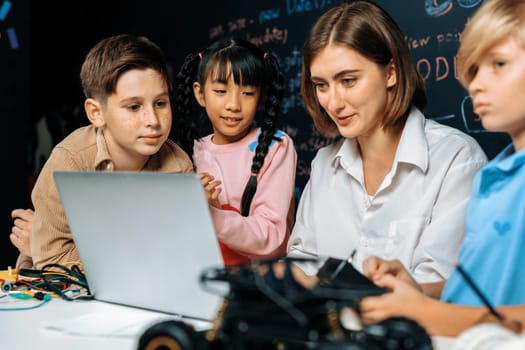 Teacher coding to demonstrate children how to code robots in the STEM class. Children fun to watch how teacher coding with confident only boy in blue shirt taking note with serious look. Erudition.