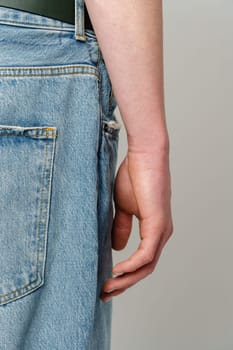 A detailed view of a person standing with their arm down, fingers slightly curled, against the backdrop of a denim blue jeans pocket. The texture of the jeans highlights the casual nature of the attire.