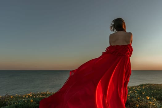 A woman in a red dress is standing in a field with the sun setting behind her. She is reaching up with her arms outstretched, as if she is trying to catch the sun. The scene is serene and peaceful