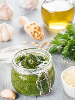 Homemade parsley pesto sauce and ingredients on gray wooden background. Close up wiev of parsley pesto in glass jar with ingredients.