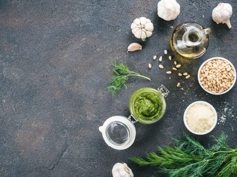 Homemade dill pesto sauce and ingredients on dark cement background. Top wiev of dill pesto in glass jar with ingredients. Copy space. Top view or flat lay.