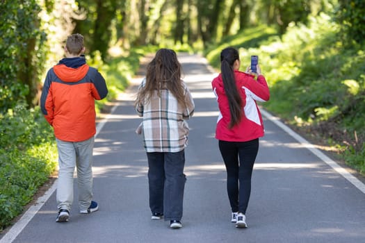 A group of friends walking along a road, moving in a straight line. They are wearing casual clothing and appear to be engaged in conversation while enjoying the outdoors together.