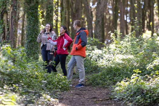 A group of friends can be seen walking together through a dense forest. The individuals are surrounded by tall trees and foliage, moving along a worn path in the wilderness.