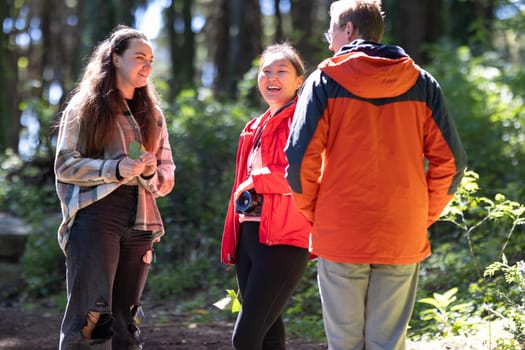 A group of friends standing together in the midst of a dense forest, surrounded by tall trees and green foliage. They appear to be talking or enjoying nature.