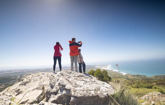 Three friends are standing together on the peak of a mountain, gazing out at the vast expanse of the ocean spread out before them. The trio appears to be enjoying the panoramic view of the sea.