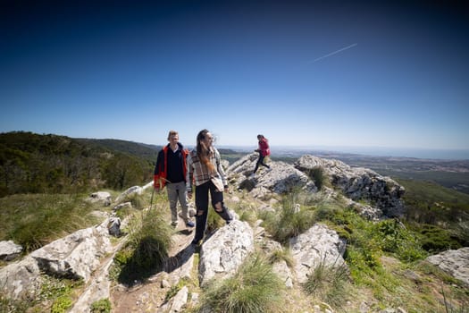 A group of friends is actively hiking up a hill, working together to conquer the challenging terrain. They are surrounded by nature, with trees and rocks visible in the background.