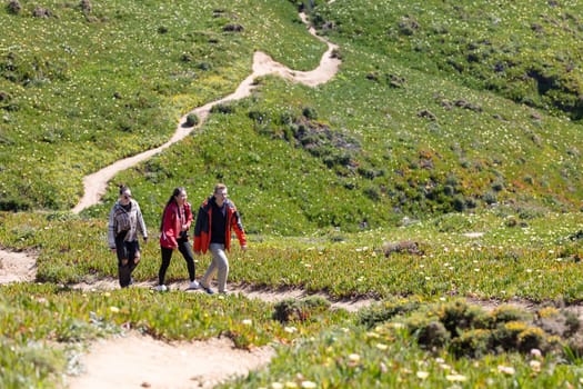 Three friends are hiking up a trail in the mountains. They are surrounded by towering peaks and lush greenery as they make their way up the path together.