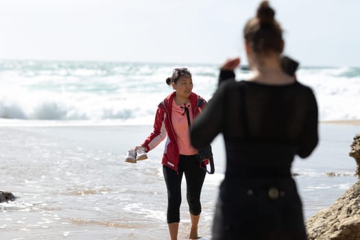 A woman is standing on the sand dunes overlooking the beach next to the ocean. She is enjoying the view of the waves crashing against the shore under the clear blue sky.