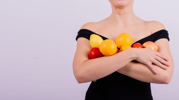 A female holding an apples, lemons, oranges in different arms isolated on grey background.