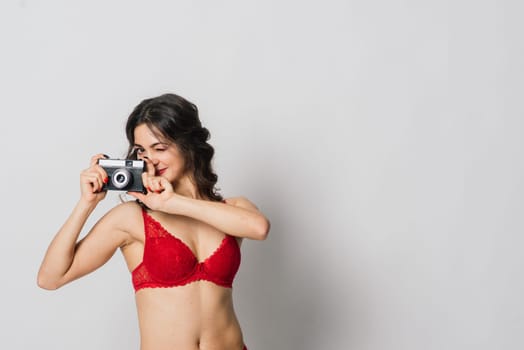 Beautiful female with pretty smile in red lingerie pinup style holding photo camera, isolated on white