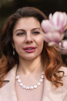 Woman magnolia flowers, surrounded by blossoming trees, hair down, wearing a light coat. Captured during spring, showcasing natural beauty and seasonal change