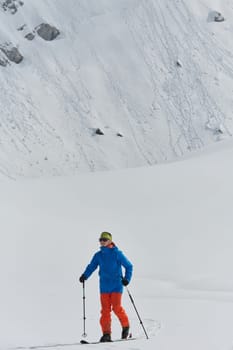 A lone skier braves the elements on a perilous climb to the top of an alpine peak.