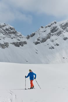 A lone skier braves the elements on a perilous climb to the top of an alpine peak.