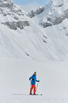 A lone skier braves the elements on a perilous climb to the top of an alpine peak.