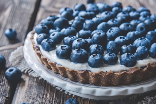 Close-up of a blueberry tart topped with fresh blueberries, beautifully arranged on a rustic wooden background, ready for serving.