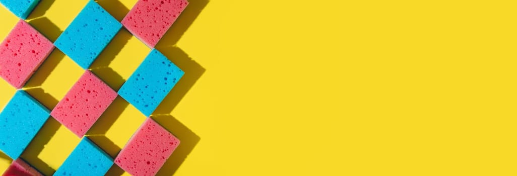 House cleaning sponges on yellow background, copy space. Flat lay or top view. Cleaning service or housekeeping concept with space. Hard shadows in sunlight. Long horizontal banner