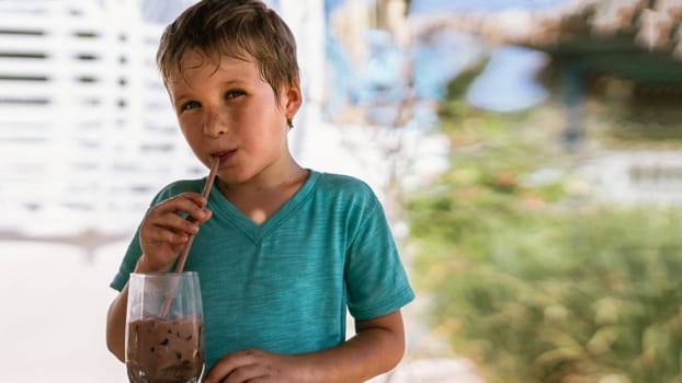 Happy childhood. Boy drinking chocolate tea with ice in hot summer day time. Cute lover of sweets and tasty things.