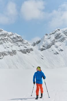 A lone skier braves the elements on a perilous climb to the top of an alpine peak.