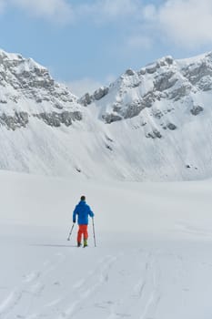 A lone skier braves the elements on a perilous climb to the top of an alpine peak.