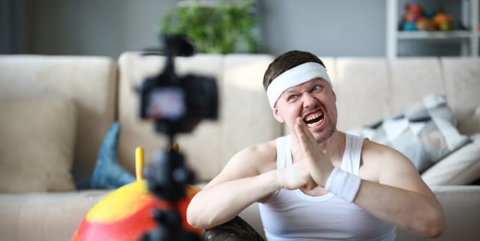 Blogger with Funny Face Record Fitness Exercise. Man Sportsman Shooting Workout on Digital Camera for Aerobic Blog. Bearded Male Training in Apartment. Guy Practice Healthy Lifestyle Photography