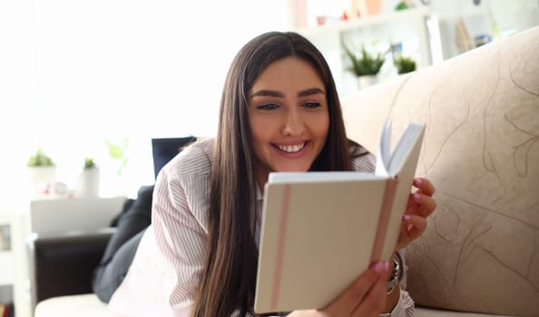 Young attractive indian teenager girl look into open book drink tea lying at couch portrait. Beautiful woman on sofa use datebook synopsis exam preparation delivery concept