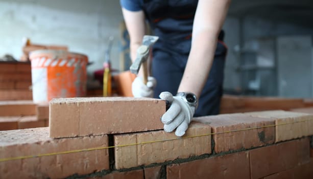 Close-up of prudent male wearing protective gloves to prevent arms from serious injuries and traumas. Man gently hammering concrete wall to achieve perfect level of smoothness. Building concept