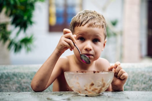 Happy childhood. Boy eating fruits with cacao spoon, summer day outside. Cute lover of sweets and tasty things .